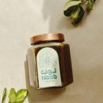 مرطبان زجاجي سداسي الشكل يحتوي على عسل سدر، مع غطاء نحاسي لامع، موضوع على سطح بيج اللون مع أوراق خضراء صغيرة في الخلفية. شعار "نوب" واضح على ملصق أبيض على المرطبان، يحيط به تصميم نباتي بسيط.